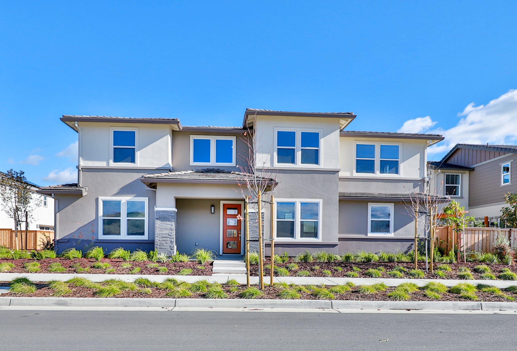 A modern two-story residential building with a well-maintained landscaped yard in the foreground, set against a clear blue sky in the background.