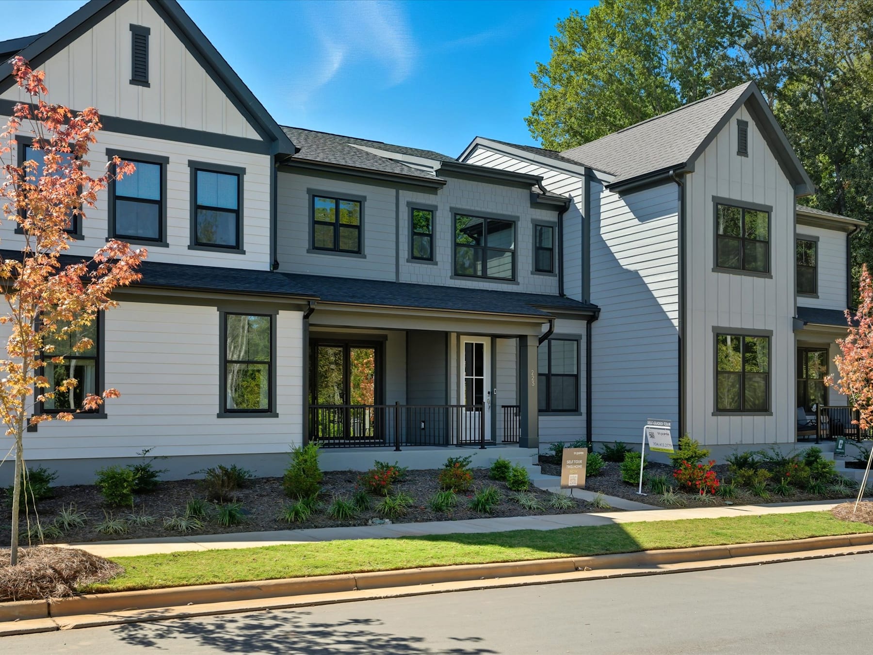 A modern, two-story residential building with a gray exterior, black trim, and large windows, surrounded by lush greenery and a well-manicured lawn in the foreground.