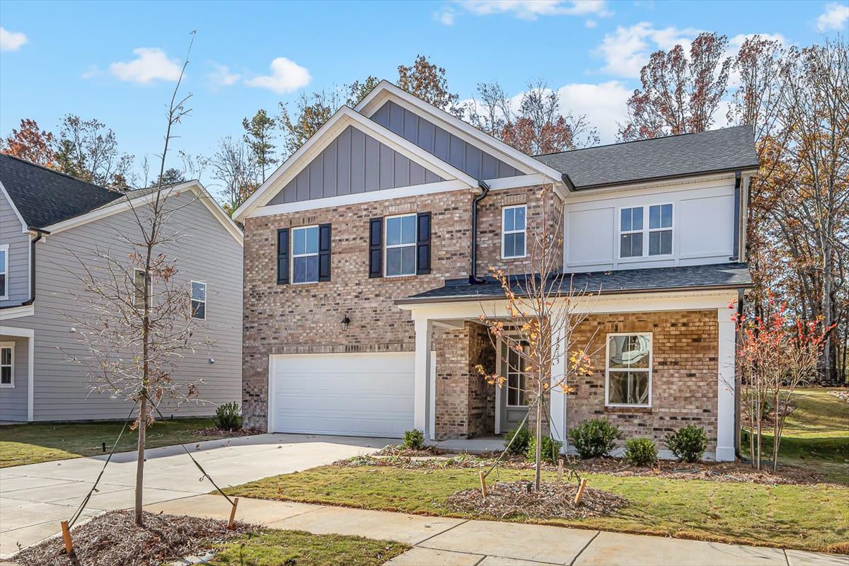 A two-story brick and siding house with a garage, surrounded by trees and a grassy lawn in a residential neighborhood.
