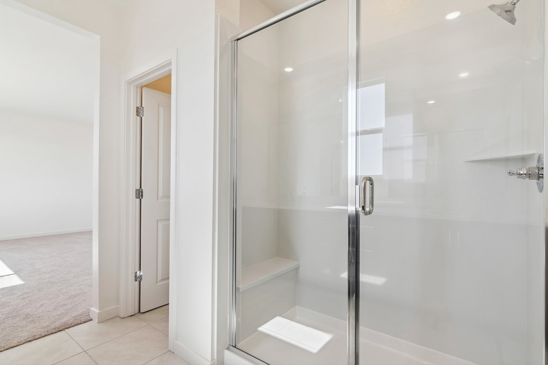 A bright, modern bathroom with a glass shower enclosure, white walls, and a wooden floor visible in the background.