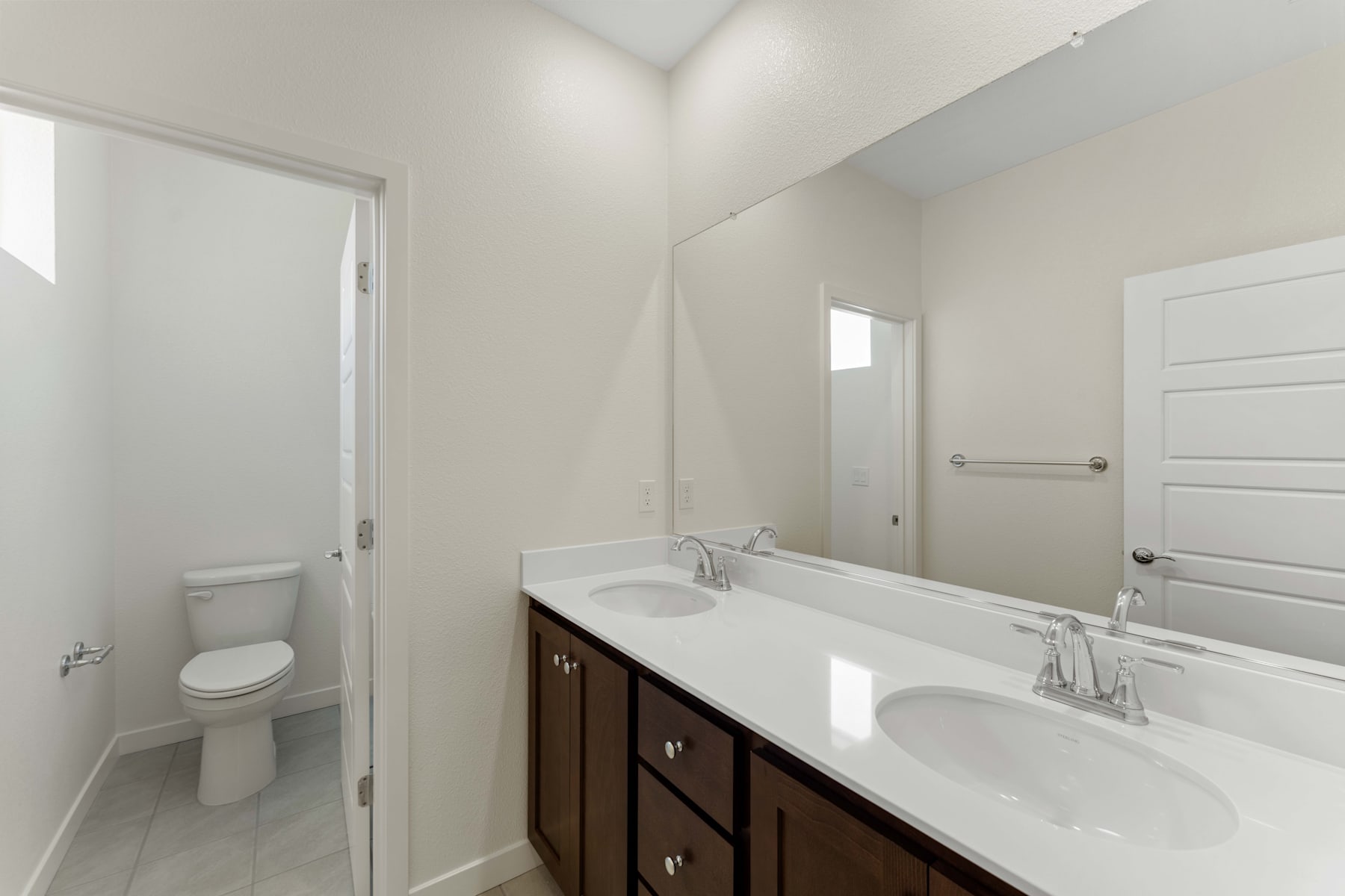 A modern bathroom with a dark wood vanity, white countertop, and a toilet visible in the background.