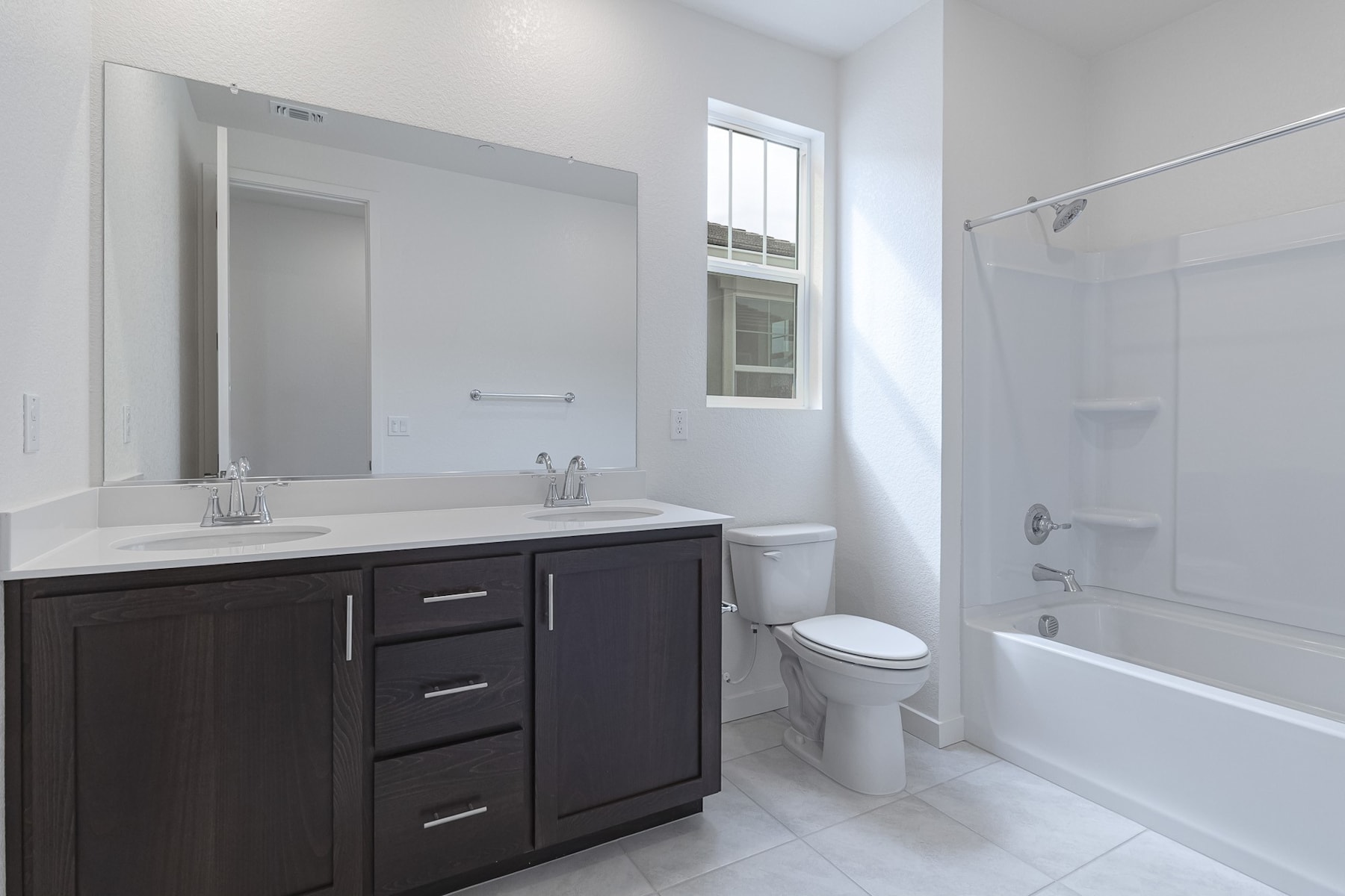A modern, well-lit bathroom with a dark wood vanity, a white sink, and a large mirror on the wall. The room also features a toilet and a bathtub with a shower curtain.