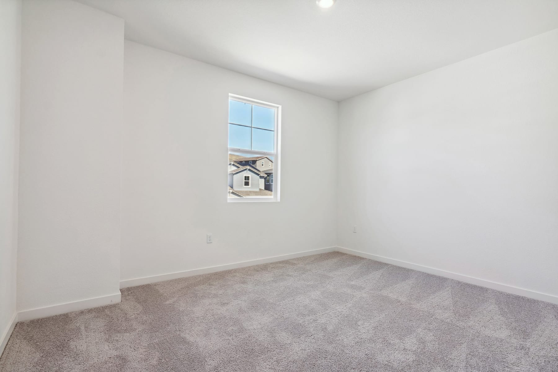 A bright, empty room with a window overlooking a residential neighborhood in the background.