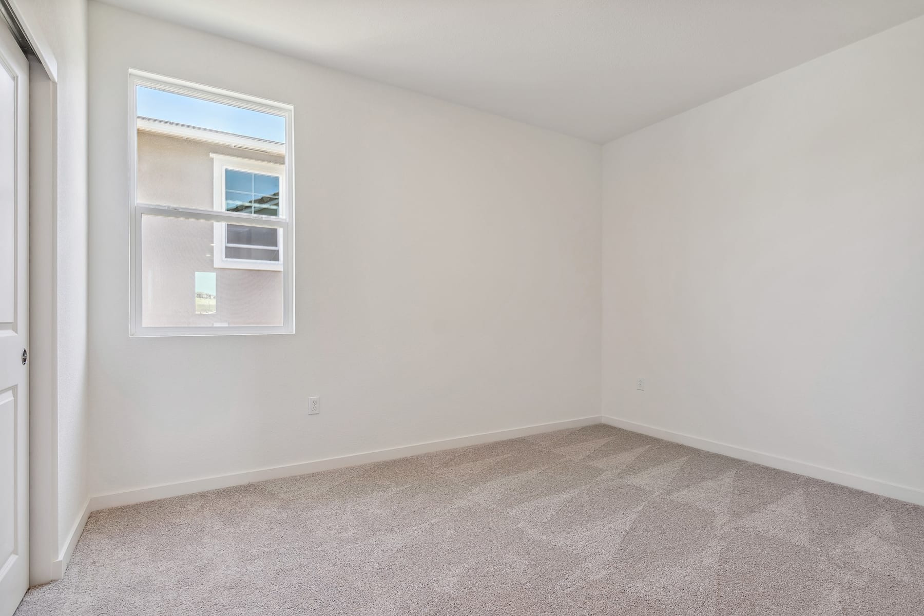 A bright, empty room with a window and light-colored carpeted floor.