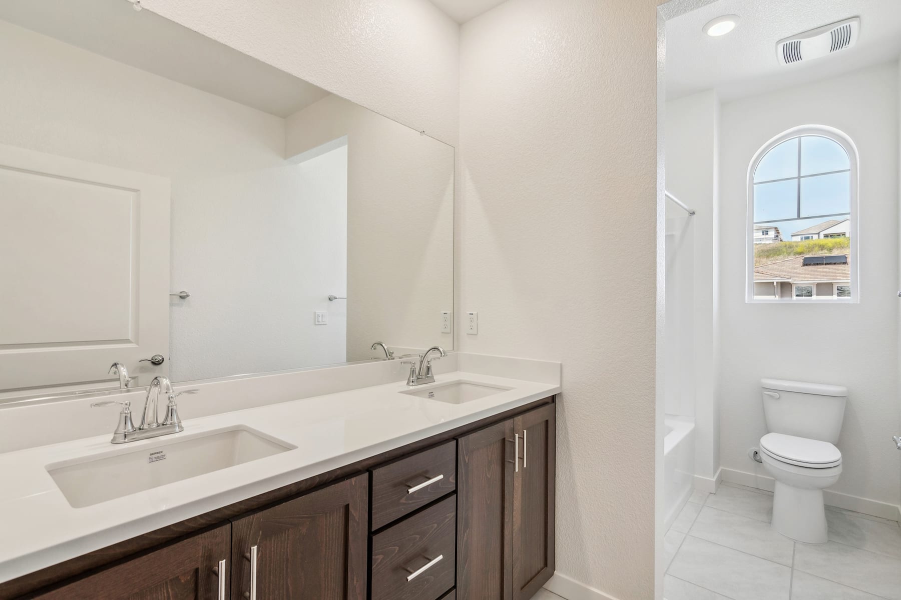 A modern bathroom with a double vanity, white countertop, and a large window providing natural light.