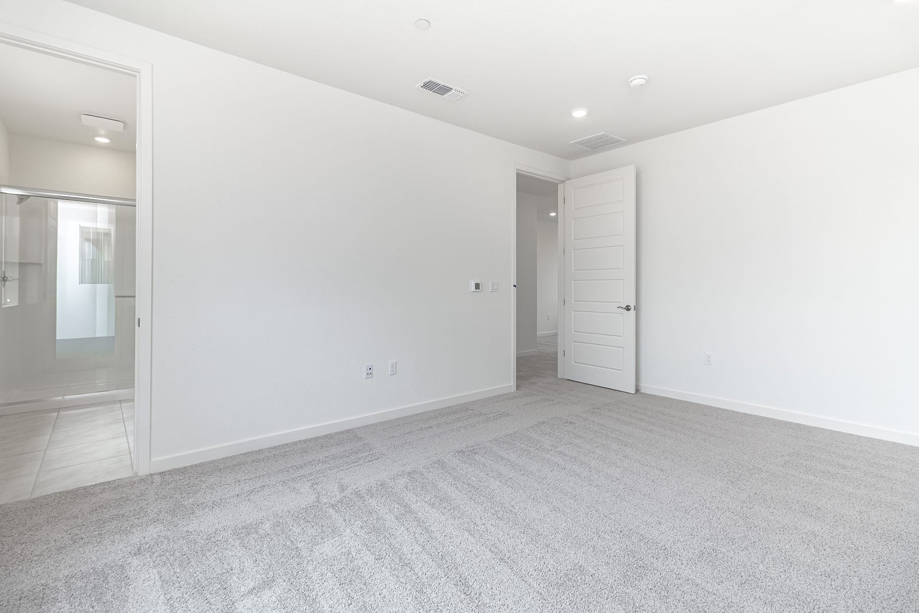 A spacious, minimalist room with white walls, a hardwood floor, and a closed door leading to another room.