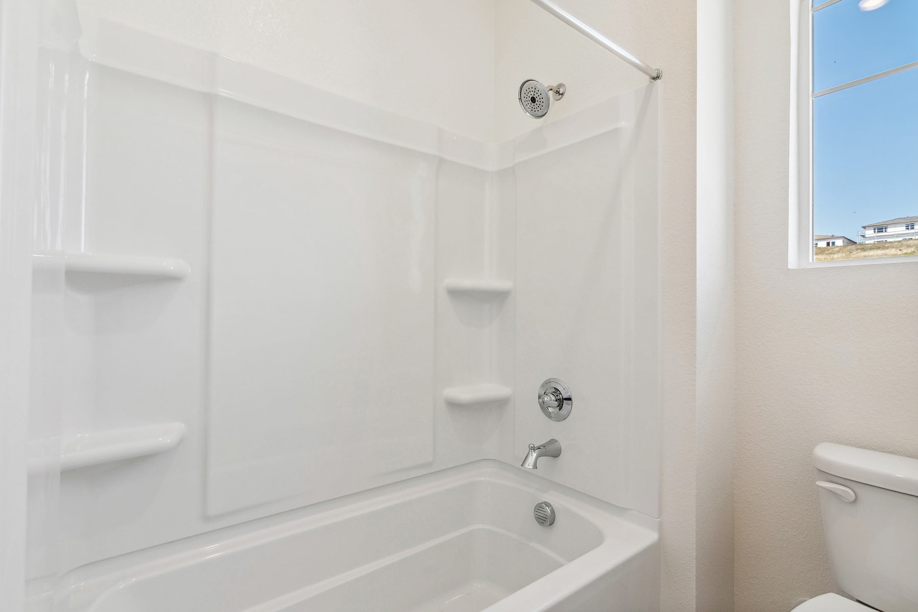 A bright, clean bathroom with a white tub, shelves, and a window providing natural light.