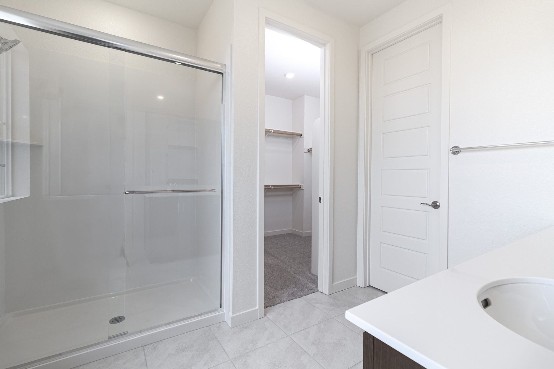 A modern, minimalist bathroom with a glass shower enclosure, white walls, and a white vanity.