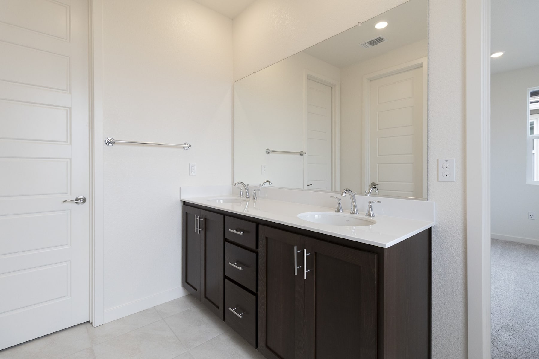 A modern bathroom with a dark wood vanity, white countertop, and a large mirror on the wall.
