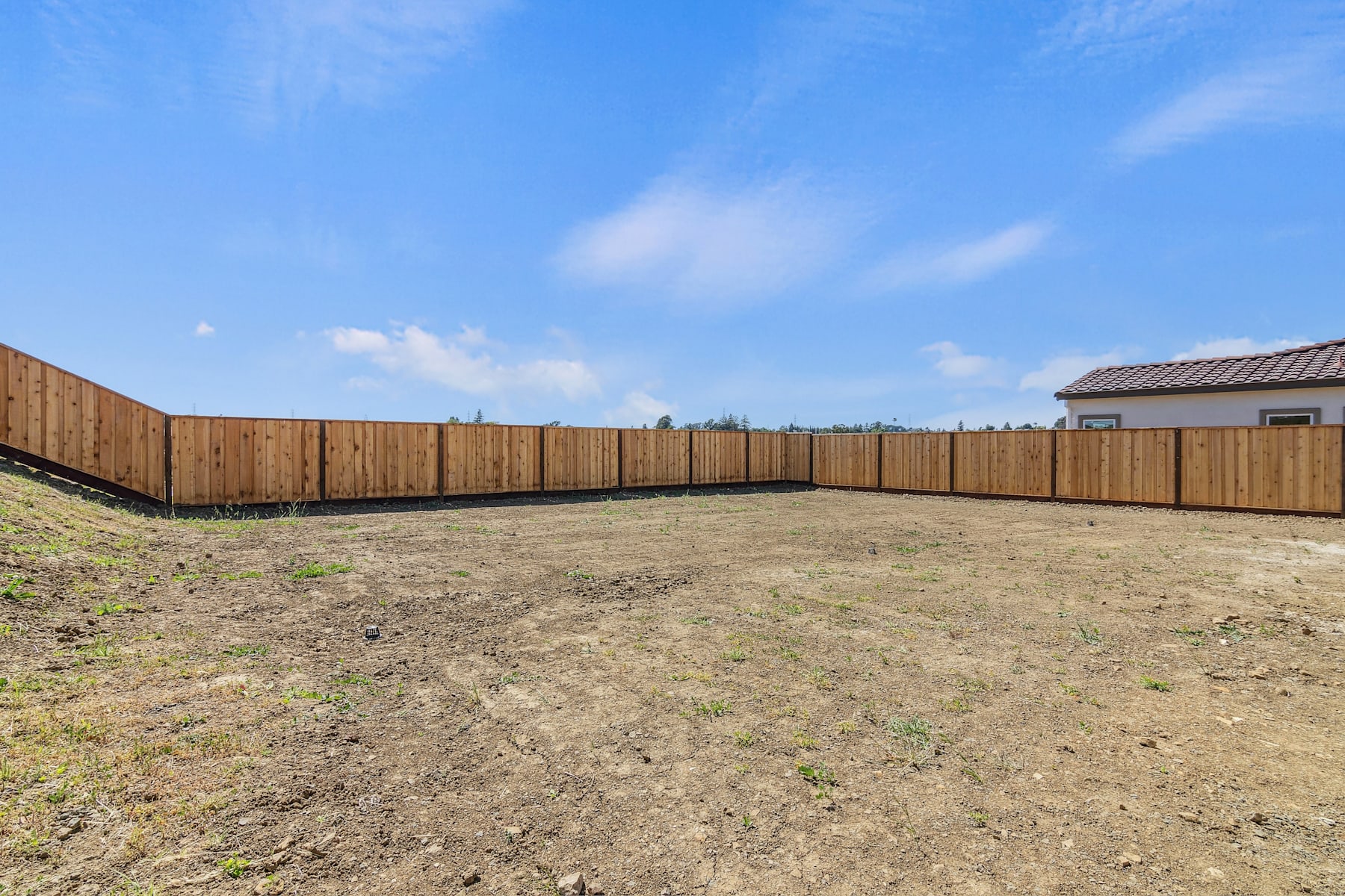 A fenced-in grassy area with a clear blue sky and scattered clouds in the background.
