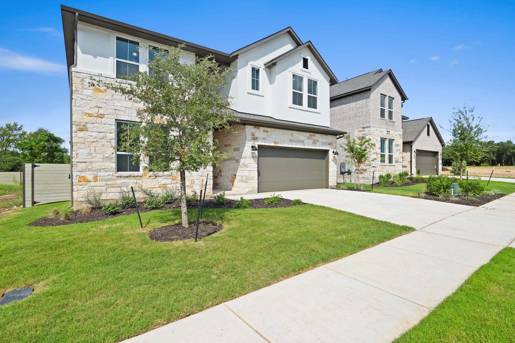 A modern, two-story residential home with a stone exterior, surrounded by a well-manicured lawn and a paved walkway leading to the front entrance.