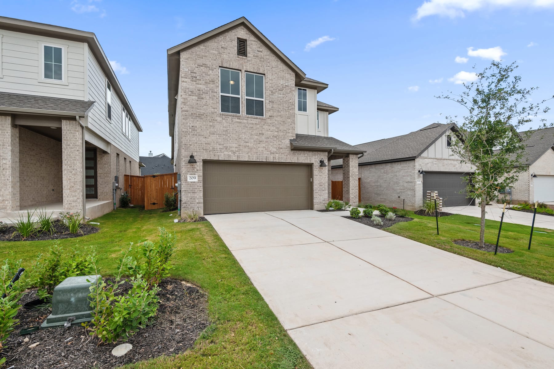 A two-story brick house with a garage, surrounded by a well-maintained lawn and landscaping, set against a clear blue sky with scattered clouds.