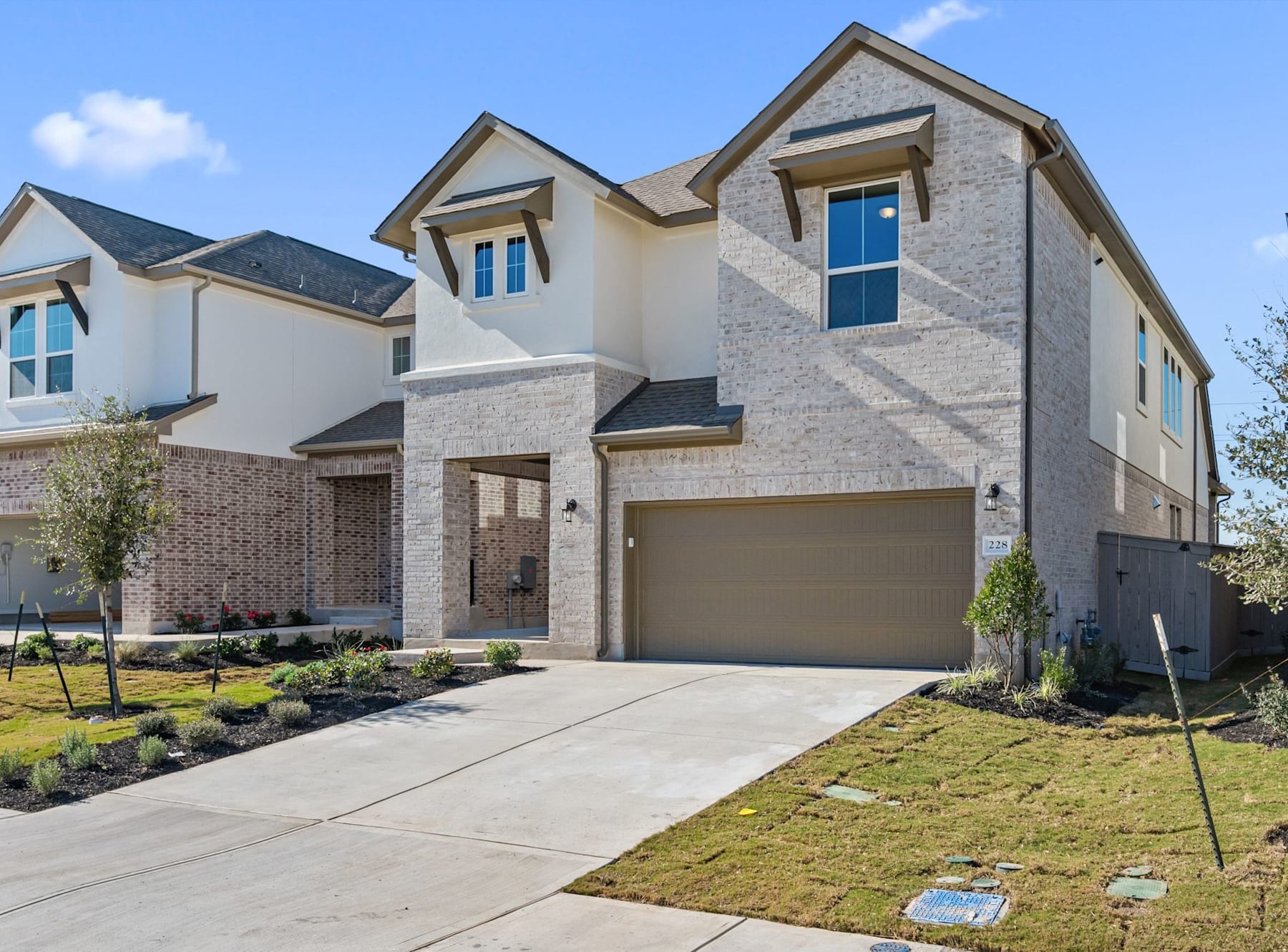 A modern, two-story residential building with a brick and stucco exterior, surrounded by a well-manicured lawn and landscaping, set against a clear blue sky with scattered clouds.