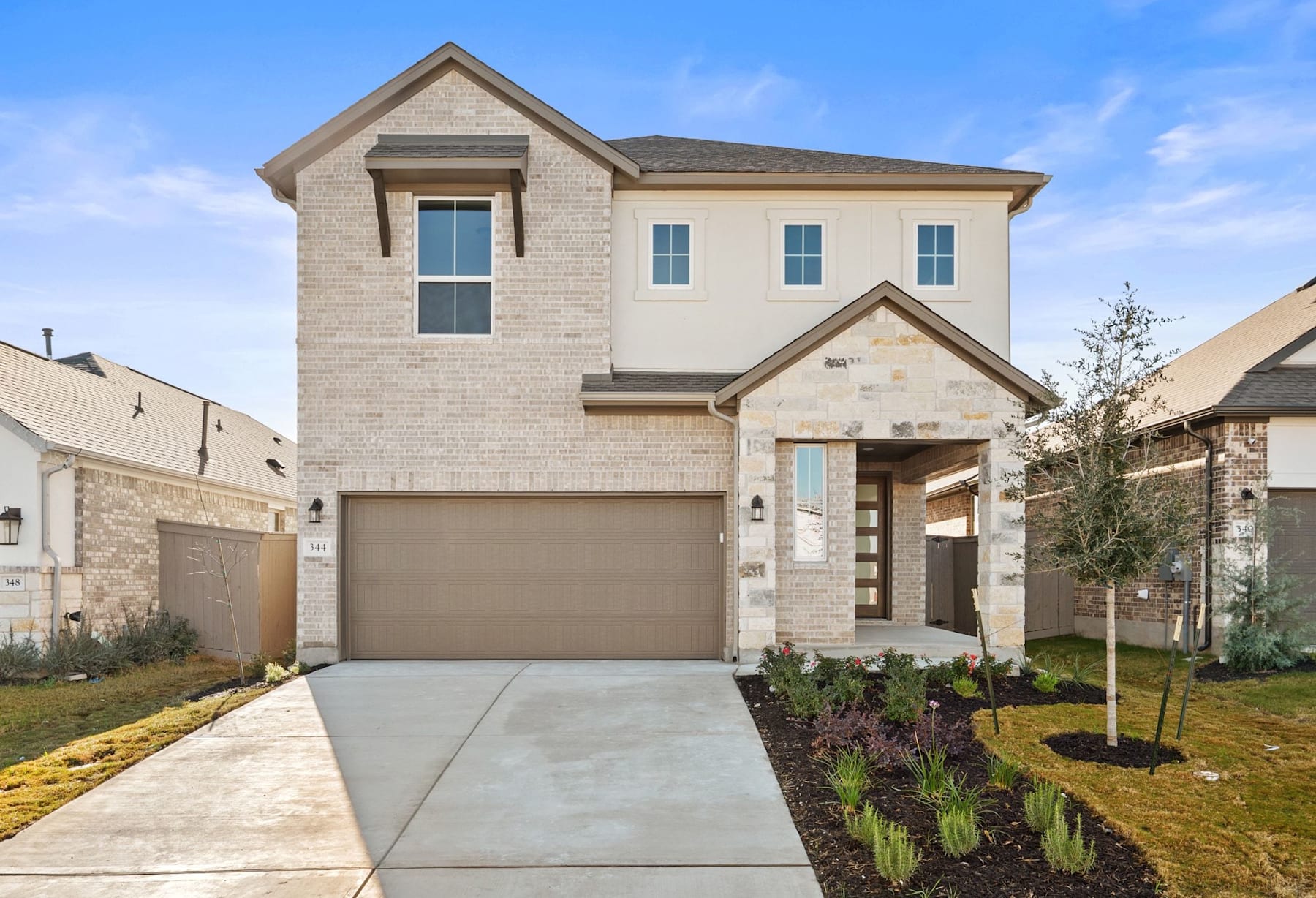 A two-story residential house with a garage, surrounded by a well-maintained lawn and landscaping, set against a clear blue sky.