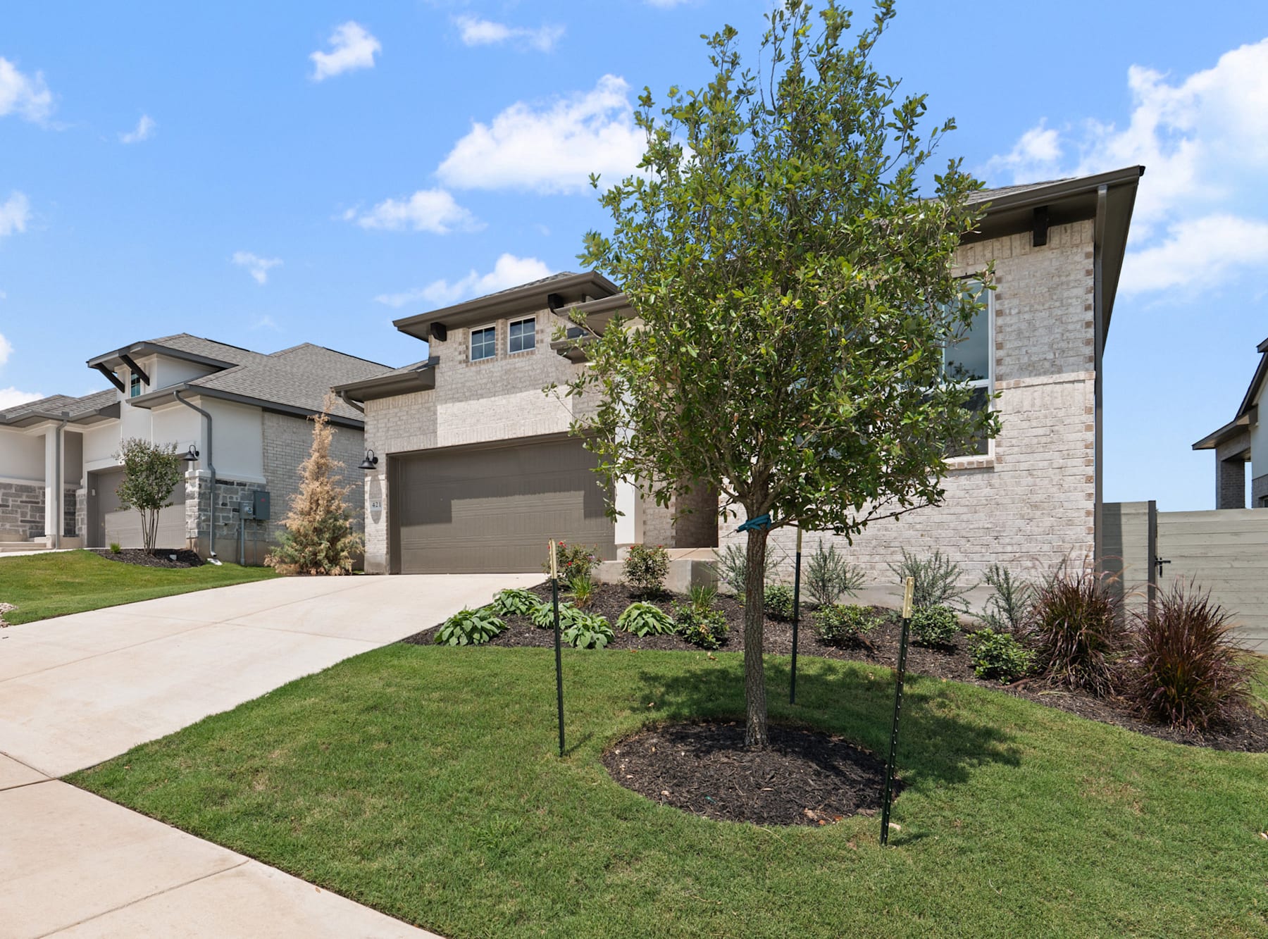 A modern, multi-story residential building with a well-manicured lawn and landscaping in the foreground, surrounded by other similar homes in a suburban neighborhood setting.