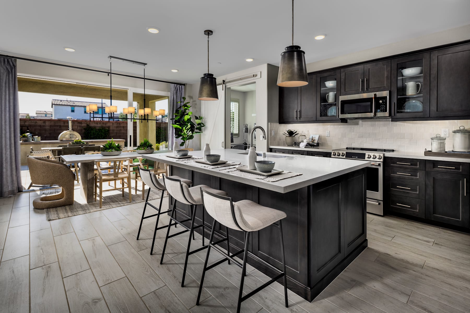 A modern and stylish kitchen with dark cabinets, a large island with bar stools, and a dining area visible in the background.