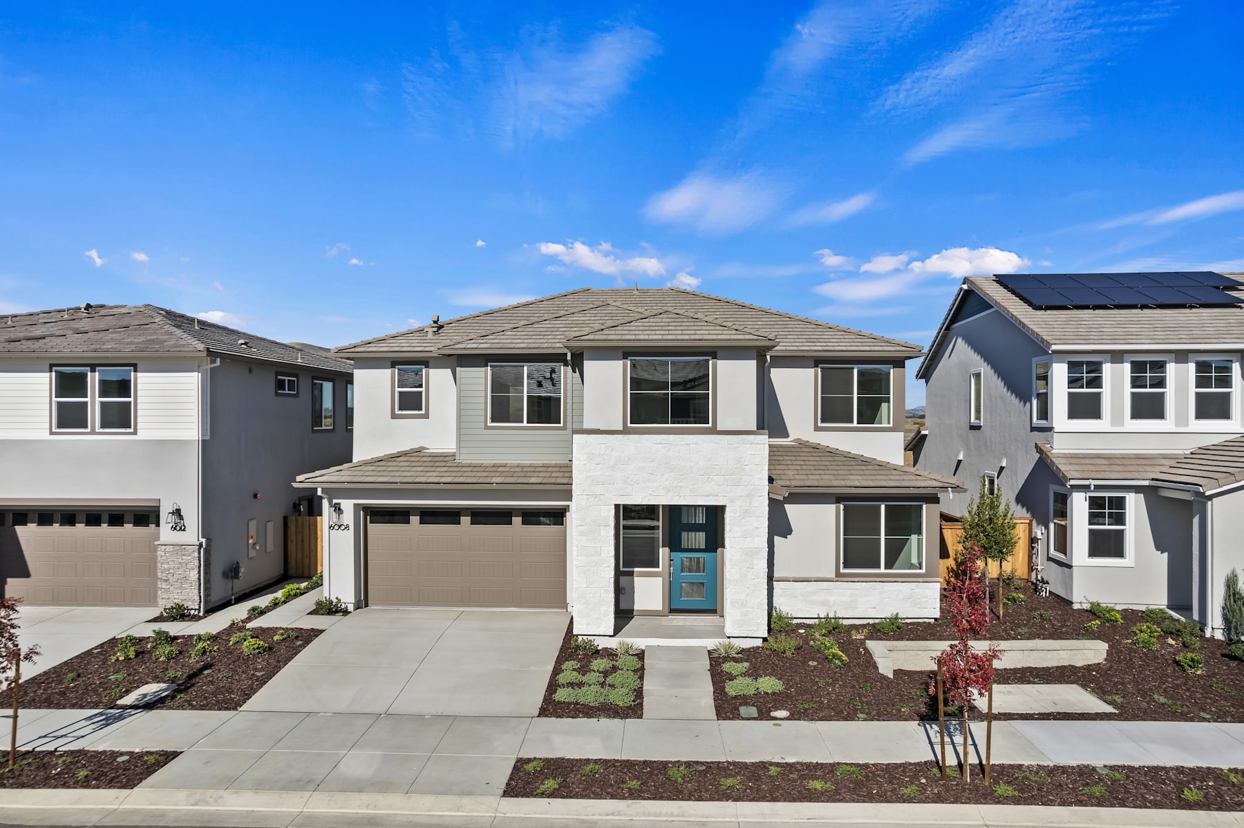 A two-story residential house with a garage, surrounded by a well-landscaped yard and a clear blue sky with wispy clouds overhead.