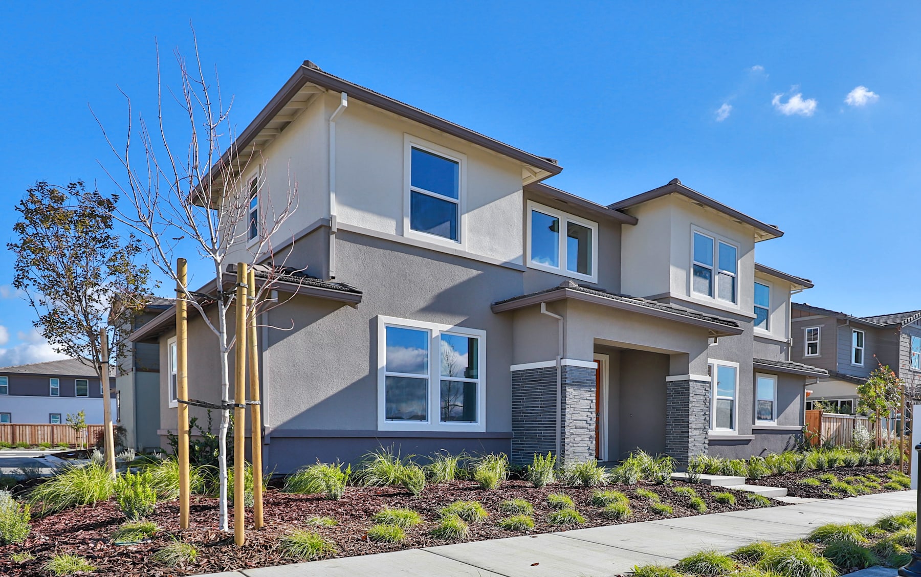 A modern two-story residential building with a gray exterior, surrounded by landscaped gardens and a clear blue sky in the background.