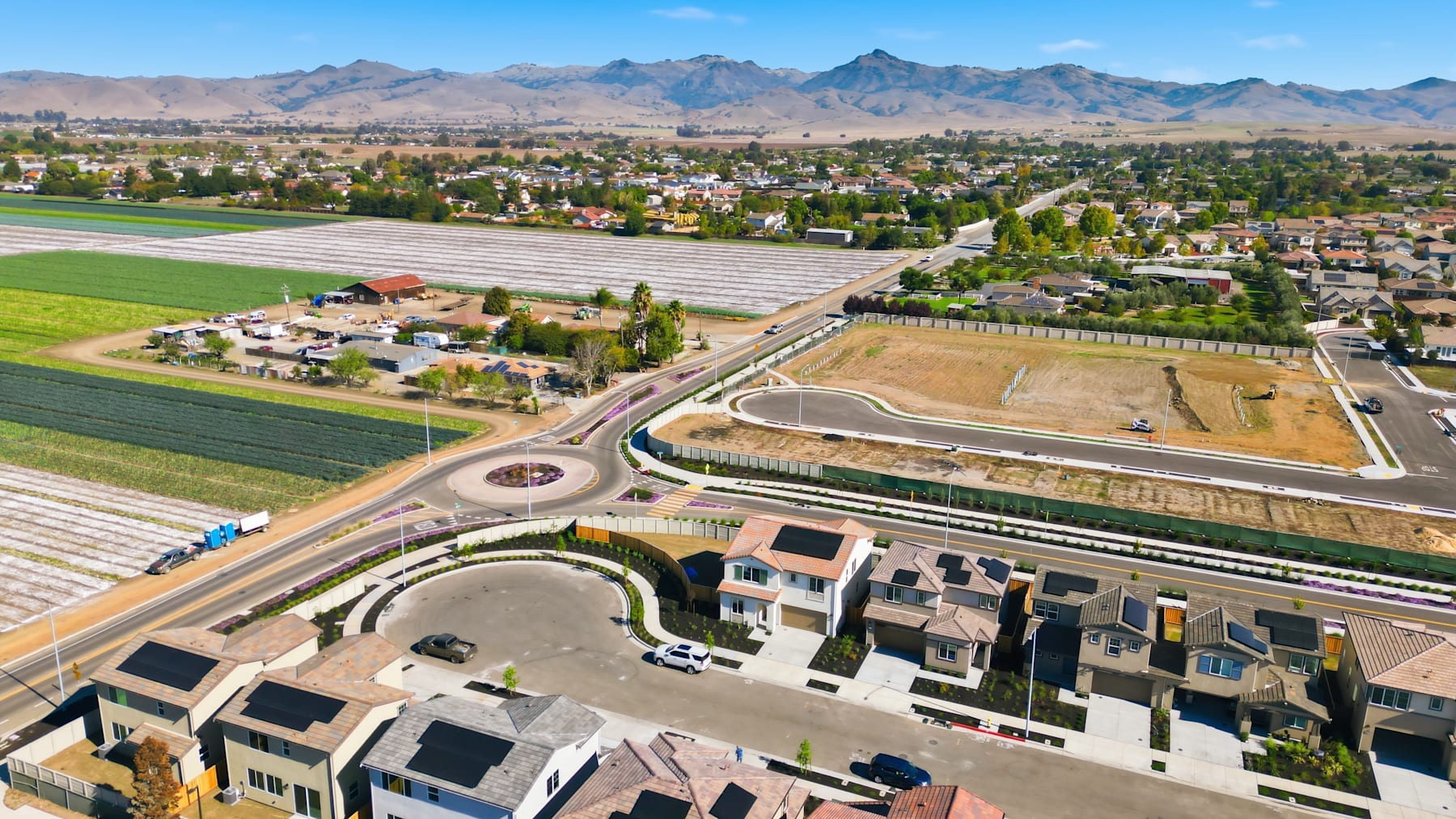 A sprawling suburban community nestled among rolling hills and towering mountains, with a mix of residential and agricultural areas visible in the foreground and background.