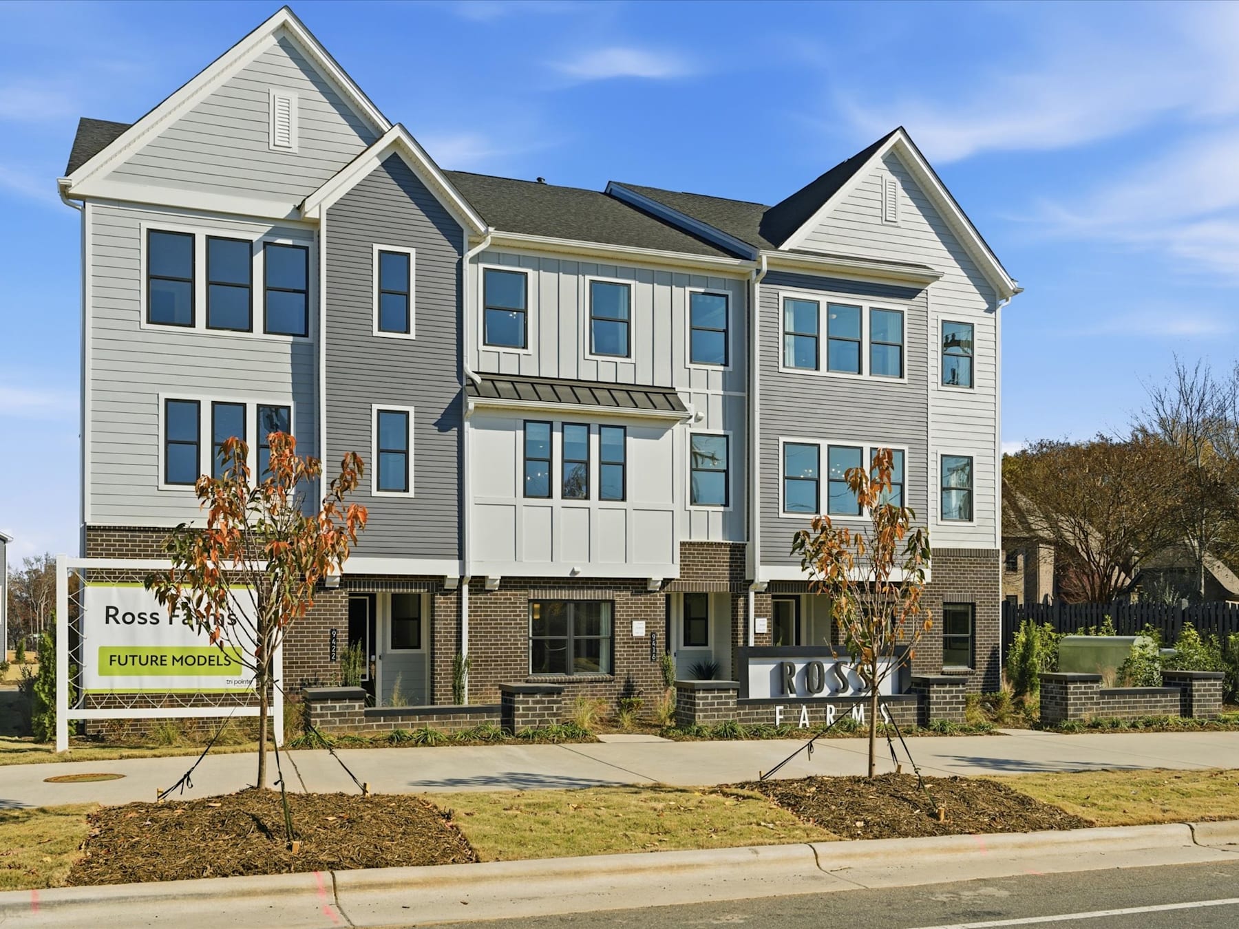 A multi-story residential building with a gray exterior, surrounded by landscaping and a sign for "Ross Park" in the foreground, set against a blue sky with some clouds.