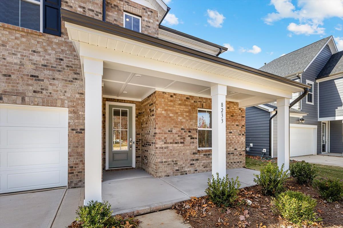 A well-maintained brick and siding home with a covered porch, surrounded by landscaping and a clear blue sky with scattered clouds.