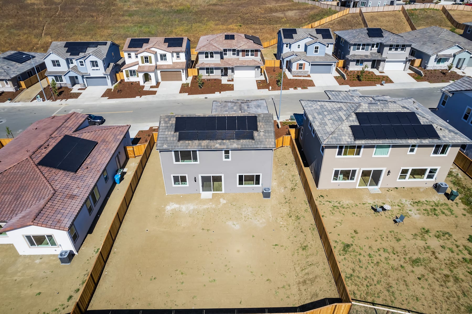 A residential neighborhood with rows of closely-spaced, two-story houses with various architectural styles and roofing materials, set against a grassy background.