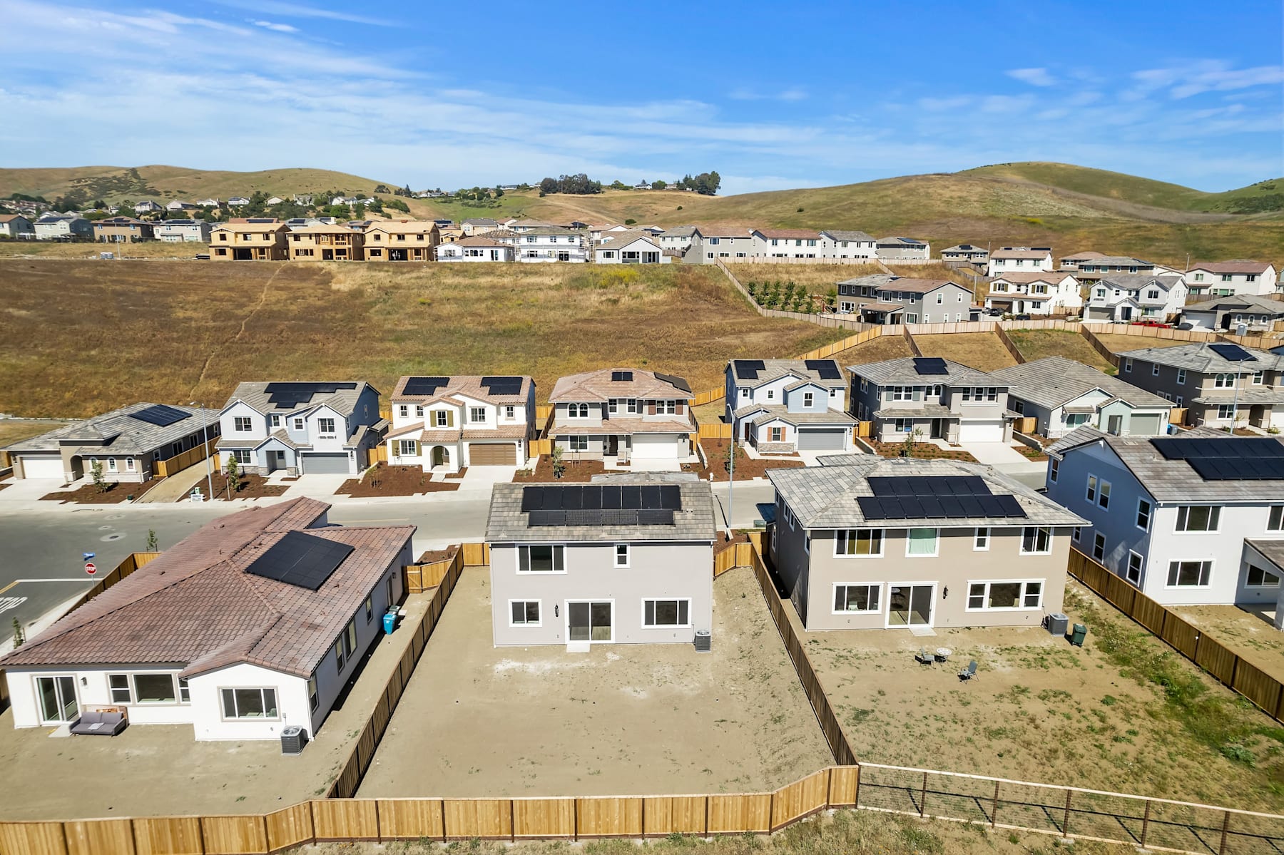 A residential neighborhood nestled in a hilly landscape, with rows of houses and buildings surrounded by open spaces and a clear blue sky.