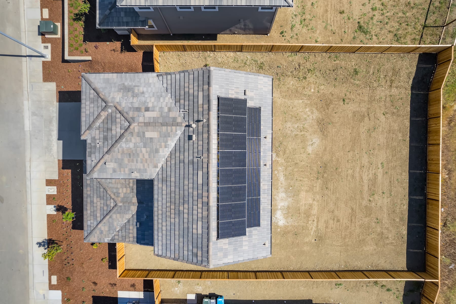 The image shows a modern, two-story residential building with a gray tiled roof, wooden accents, and a grassy yard in the foreground.