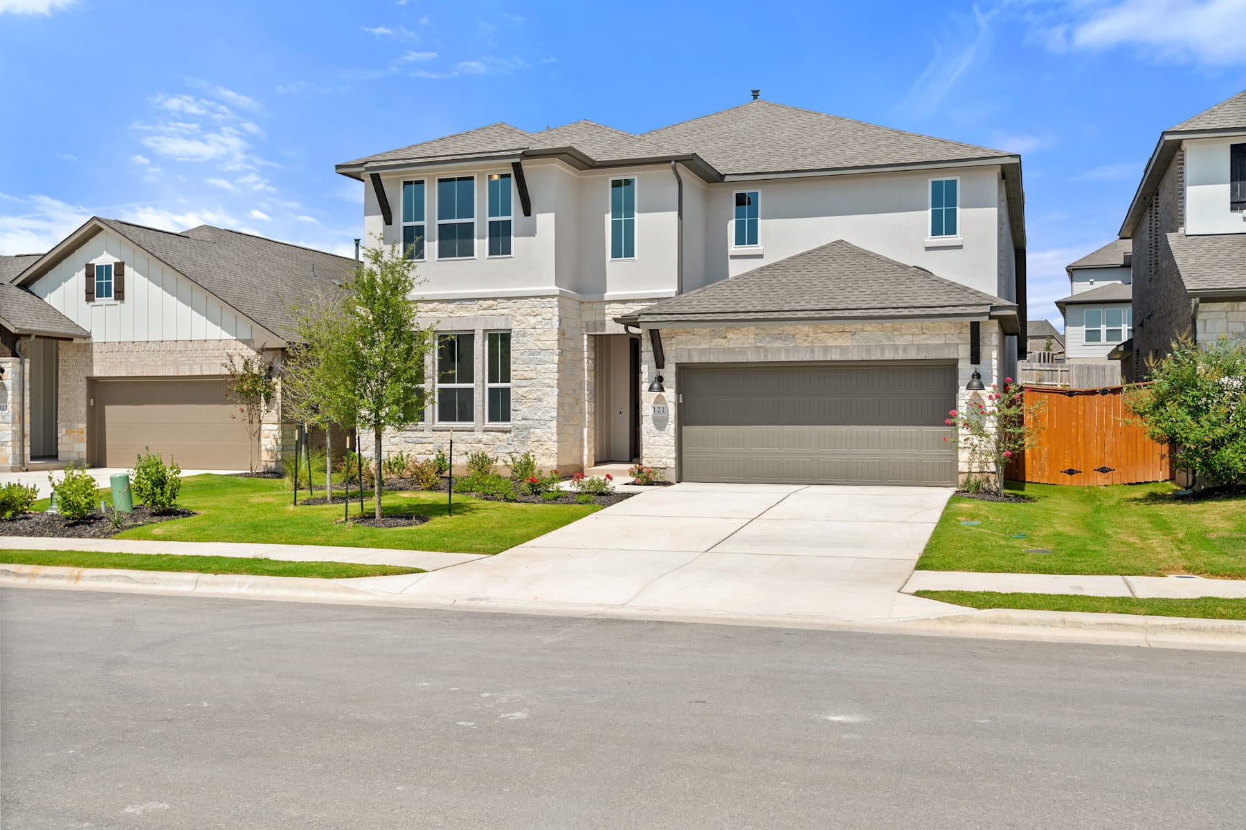 A two-story residential house with a garage, surrounded by a well-manicured lawn and other houses in a suburban neighborhood.