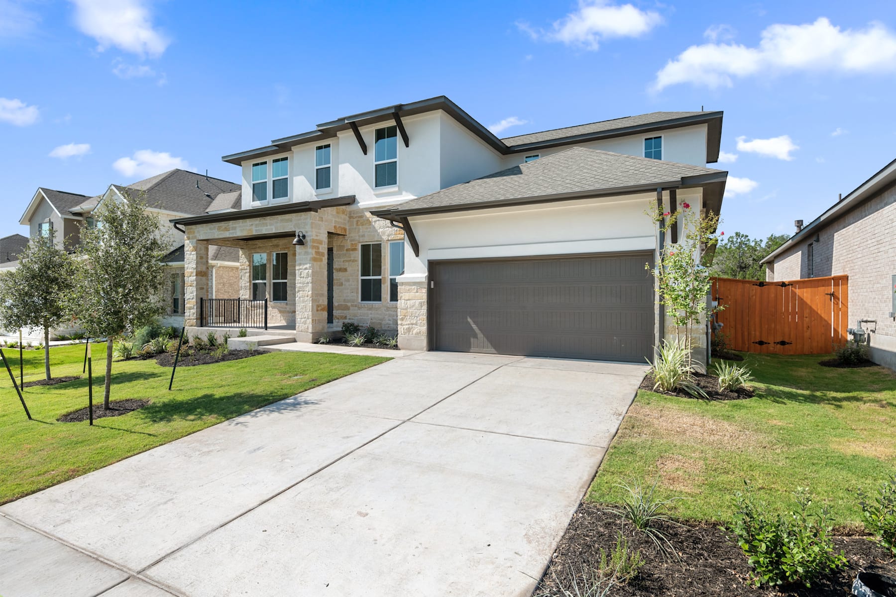 A two-story residential house with a garage, surrounded by a well-maintained lawn and landscaping, set against a clear blue sky with scattered clouds.
