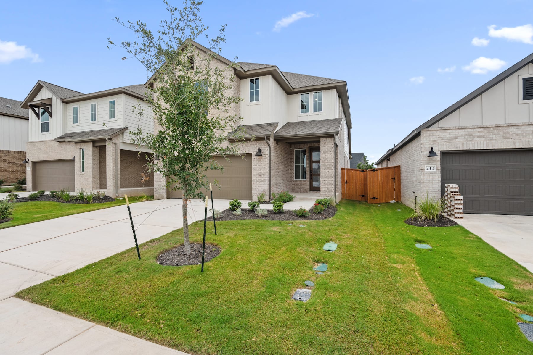 A well-manicured lawn with a paved walkway leads to a two-story residential home with a garage, surrounded by lush greenery and a clear blue sky.