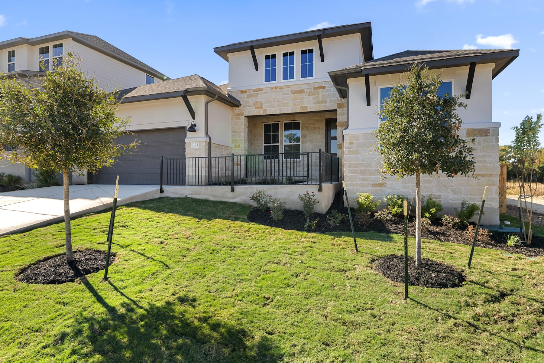 A modern, two-story residential home with a well-manicured lawn and landscaping in the foreground, set against a clear blue sky in the background.