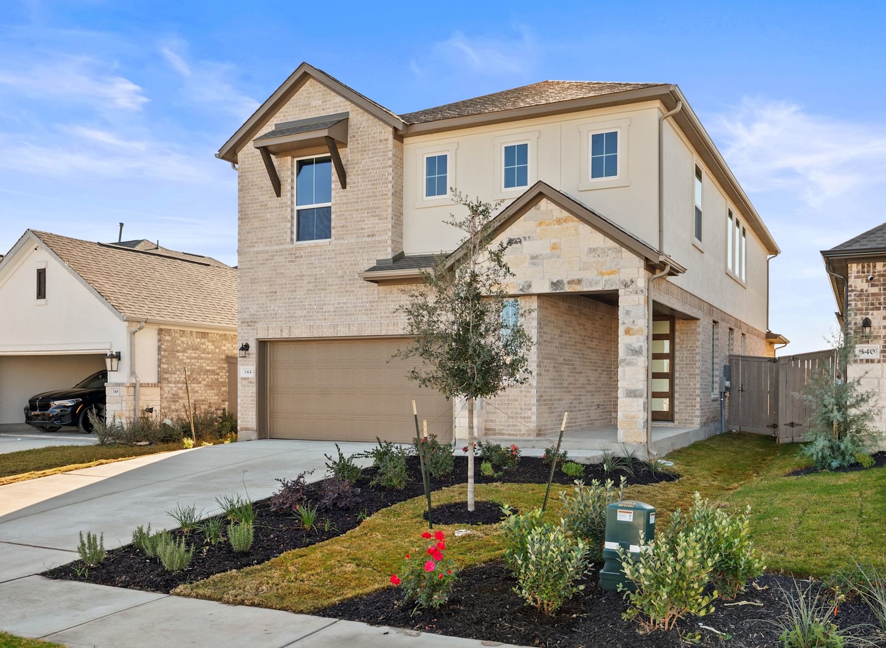 A two-story residential house with a brick exterior, surrounded by a well-maintained landscaped yard featuring various plants and shrubs.