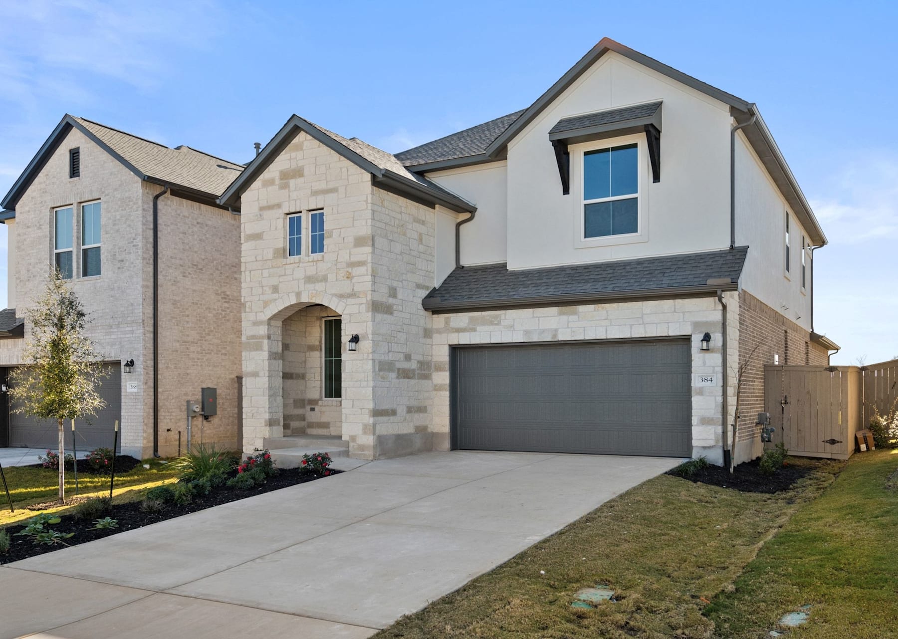 A two-story residential house with a garage, surrounded by a well-manicured lawn and landscaping, set against a clear blue sky.