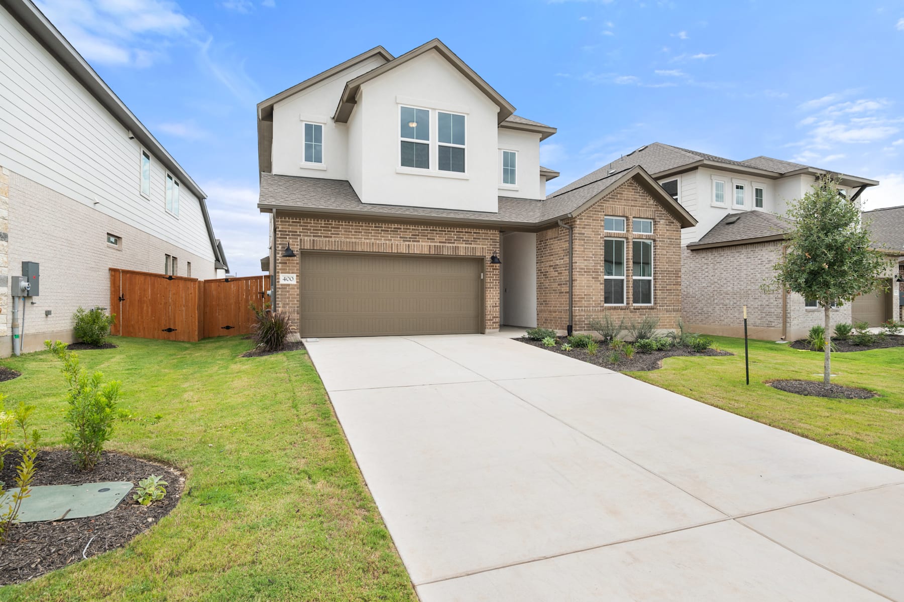 A two-story residential house with a brick and siding exterior, surrounded by a well-manicured lawn and landscaping, set against a clear blue sky.