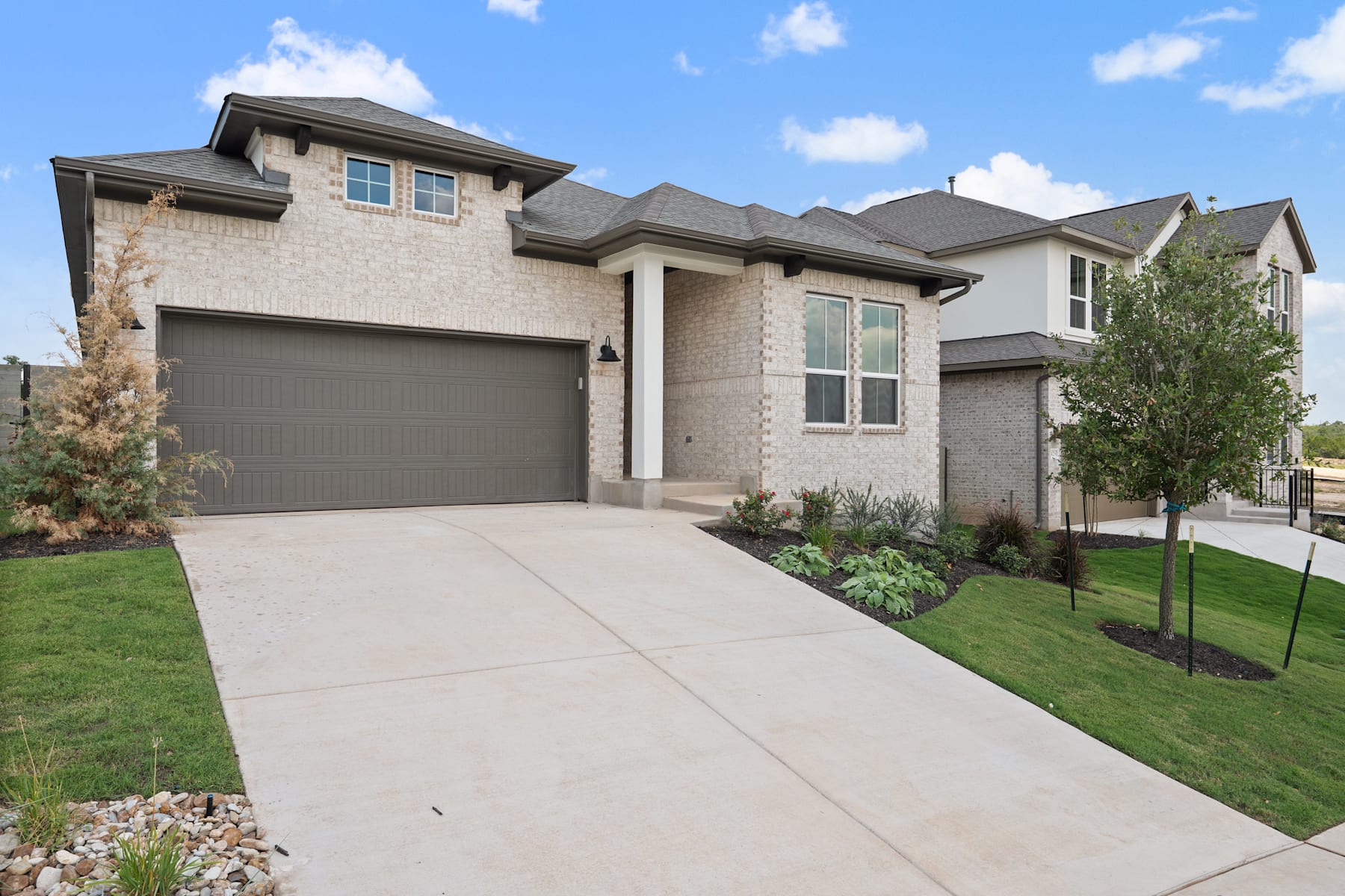 A two-story brick and stone house with a garage, surrounded by a well-manicured lawn and landscaping, set against a blue sky with fluffy white clouds.