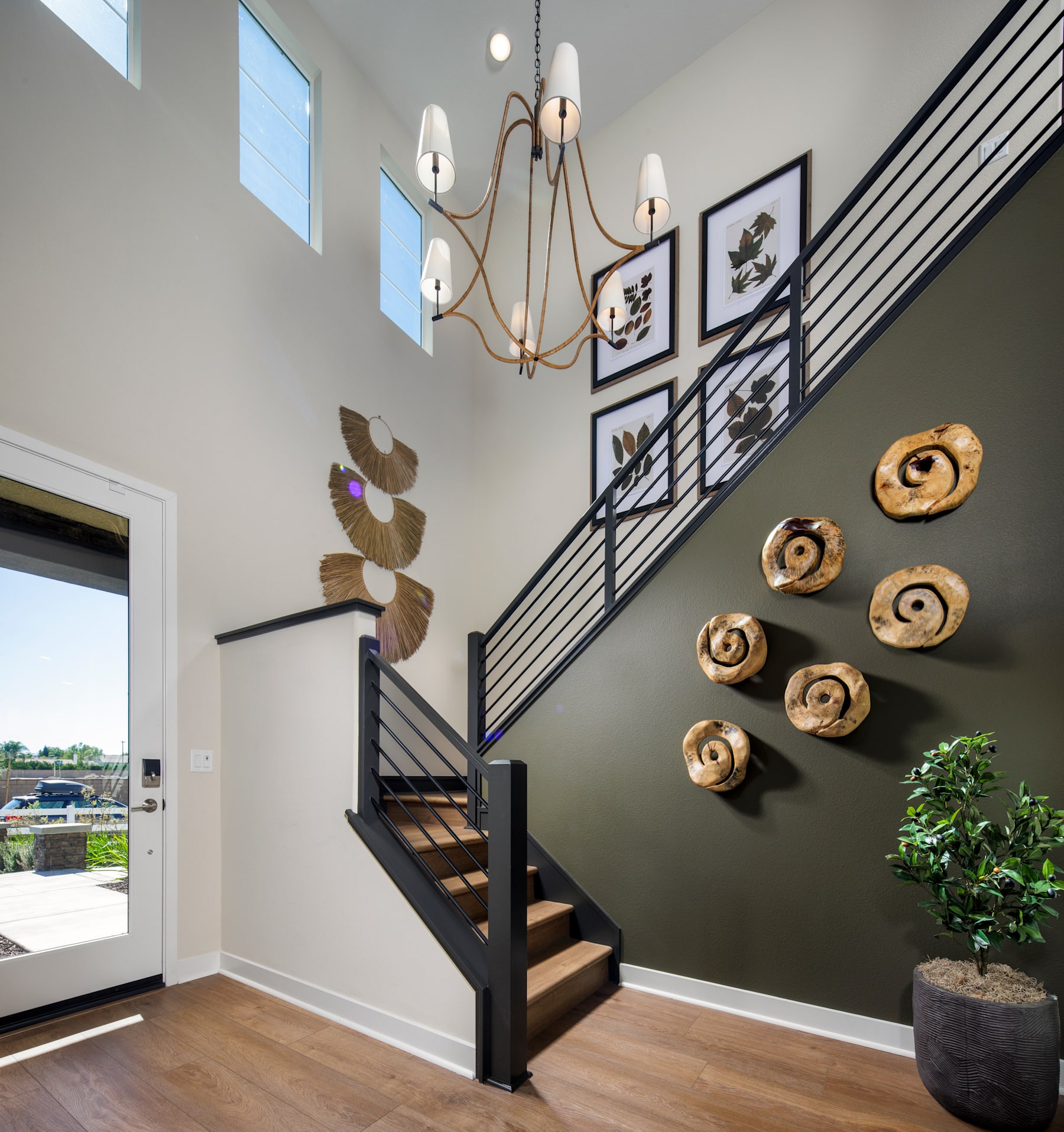 A modern and stylish entryway with a wooden staircase, a decorative chandelier, and various wall art and decor elements, creating a visually appealing and inviting space.