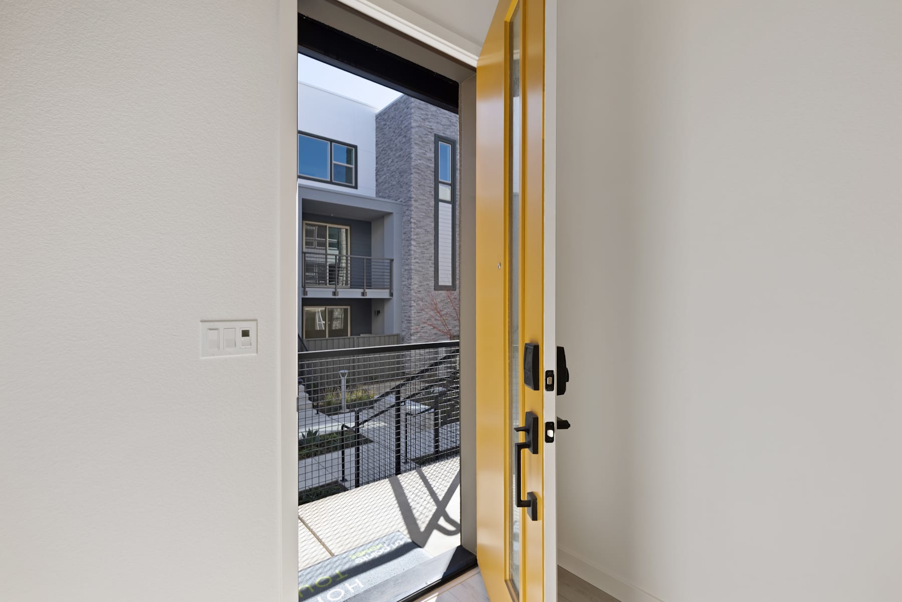 A partially open yellow door reveals a view of a modern building exterior with gray walls, windows, and a metal railing in the background.