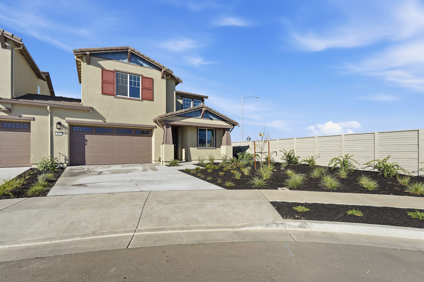 A modern two-story residential building with a landscaped front yard and a clear blue sky in the background.