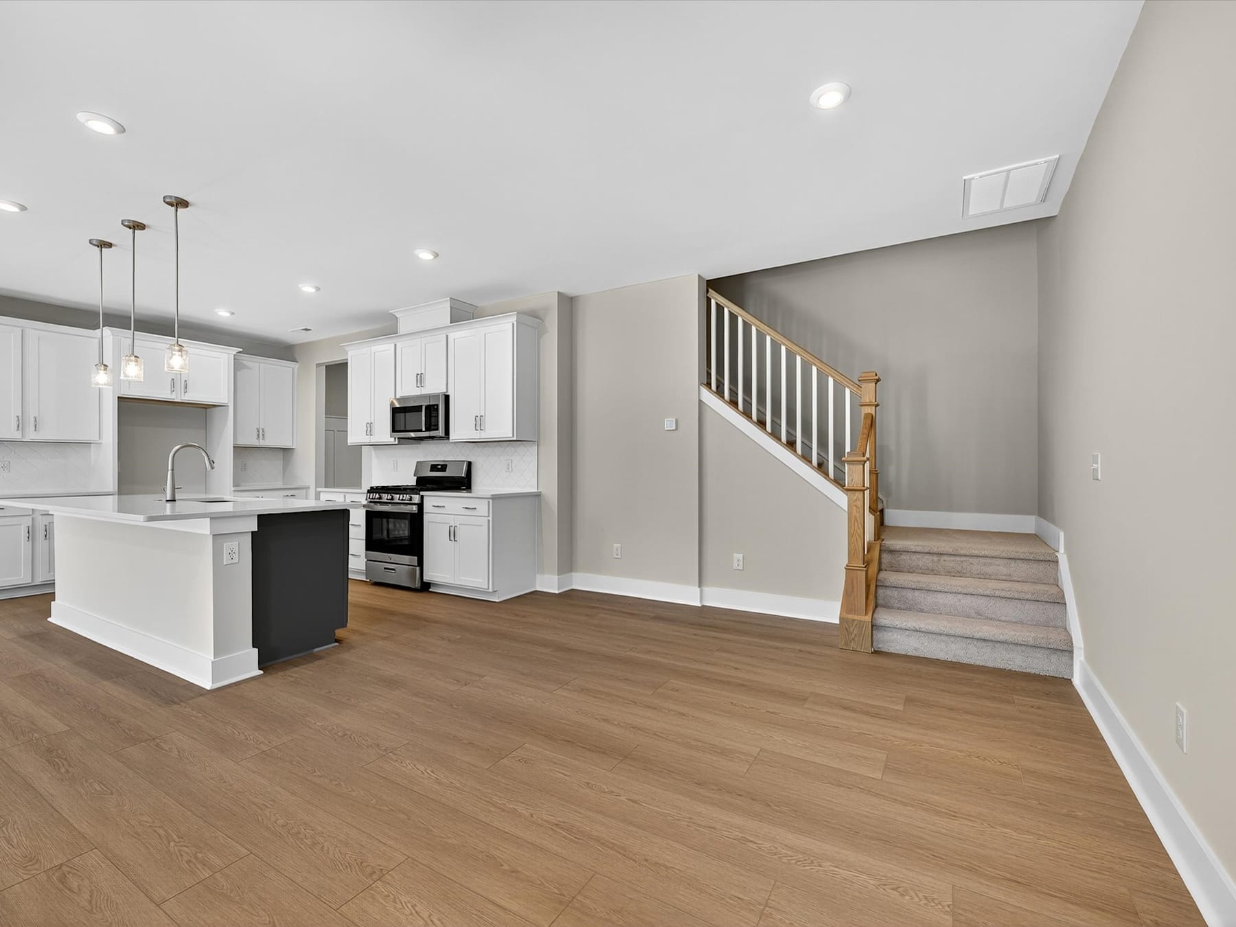 A modern, open-concept kitchen and living space with white cabinets, hardwood floors, and a wooden staircase leading to the upper level.