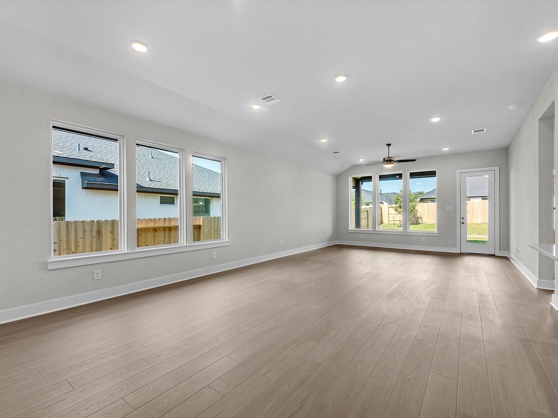 A spacious, well-lit room with hardwood floors, large windows, and recessed lighting, providing a bright and open living space.