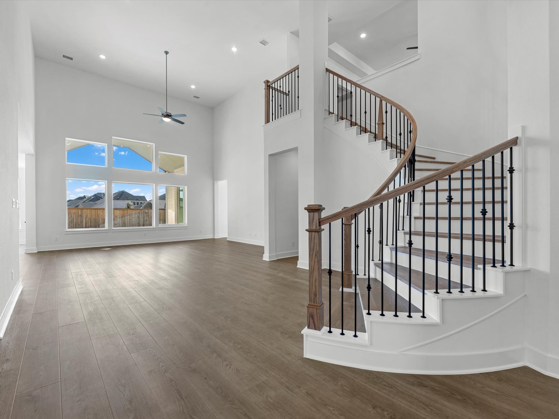 A spacious and bright interior with a wooden staircase, hardwood floors, and large windows overlooking a scenic outdoor landscape.