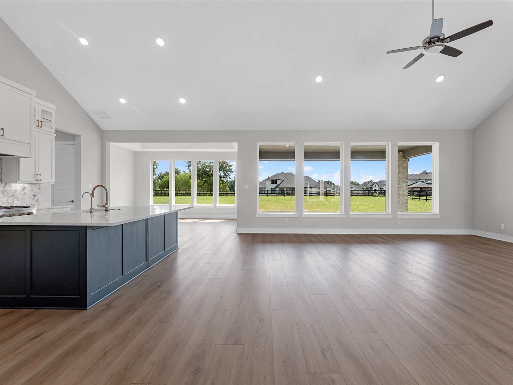 A spacious and bright open-concept living area with a kitchen, hardwood floors, and large windows overlooking a scenic outdoor landscape.