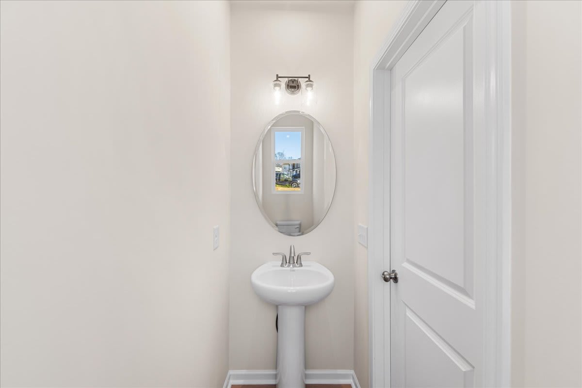 A small, minimalist bathroom with a white pedestal sink, a mirror, and a window providing natural light.