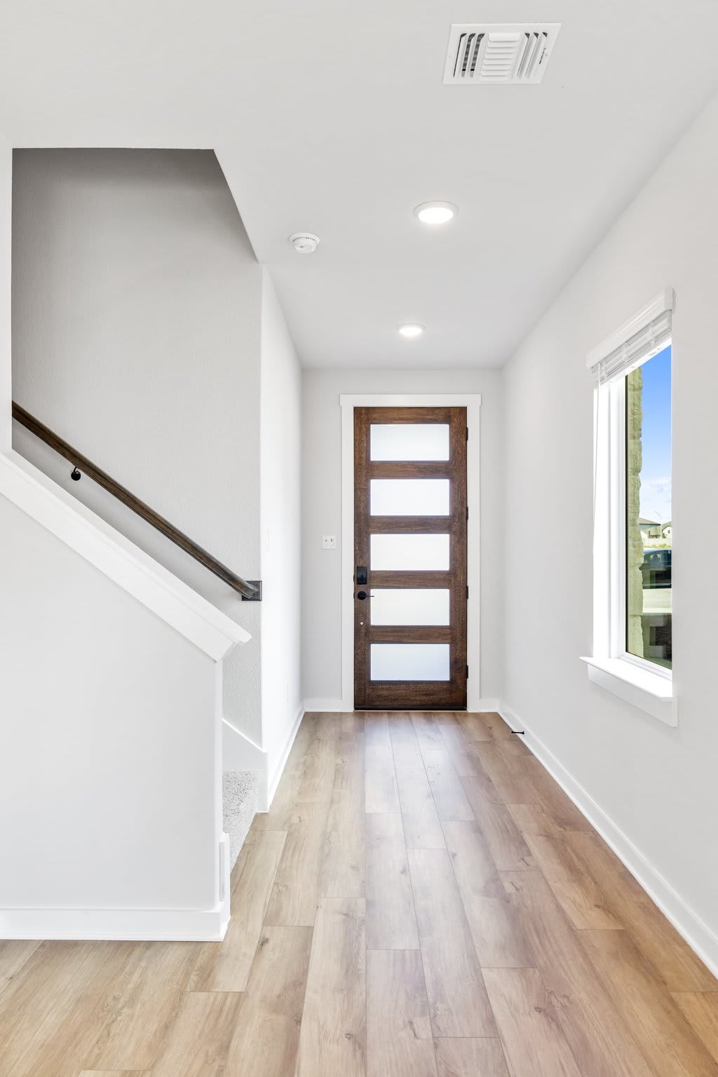 A bright and spacious entryway with a wooden door, hardwood floors, and a staircase leading upstairs.