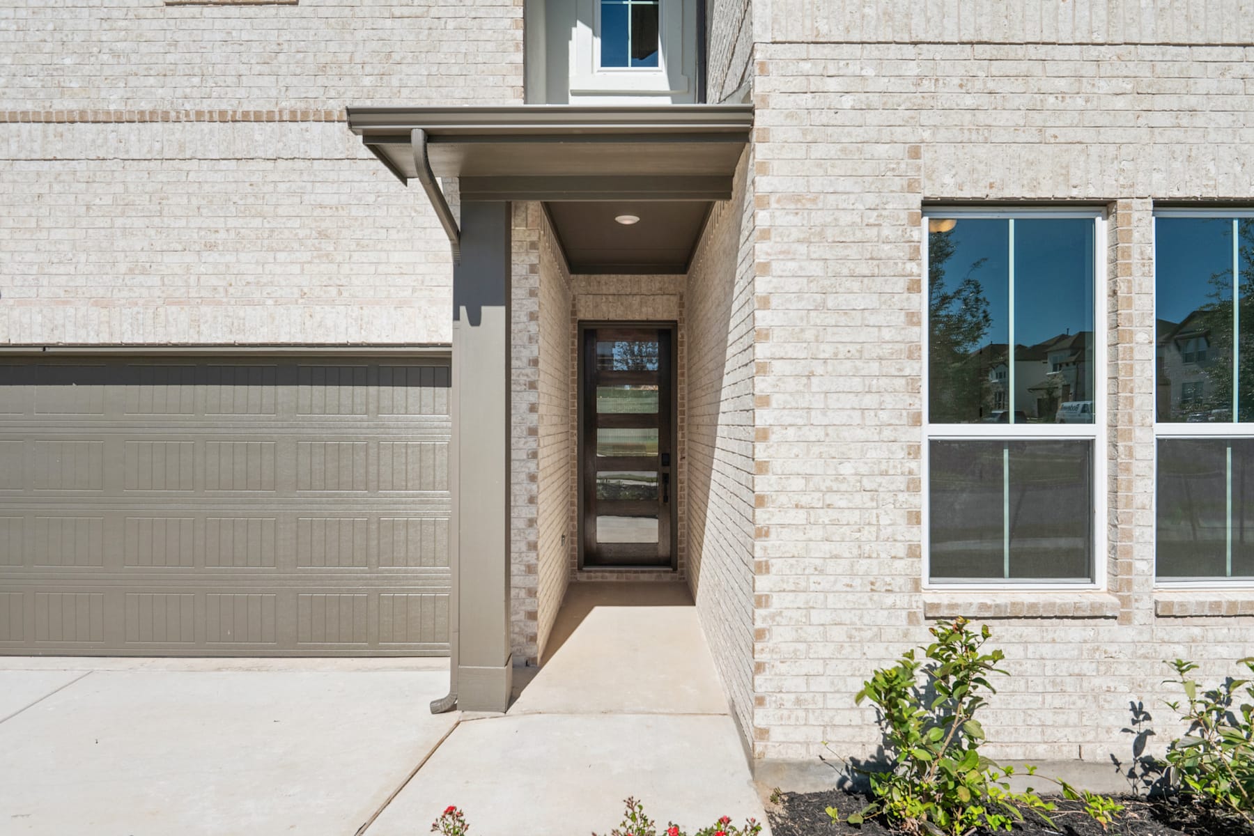A modern, two-story brick building with a garage door, a covered entryway, and large windows overlooking a paved driveway and landscaped yard.