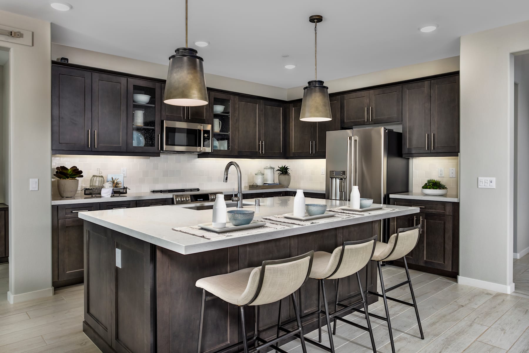 A modern and stylish kitchen with dark wood cabinets, a large island with a white countertop, and pendant lights hanging above.