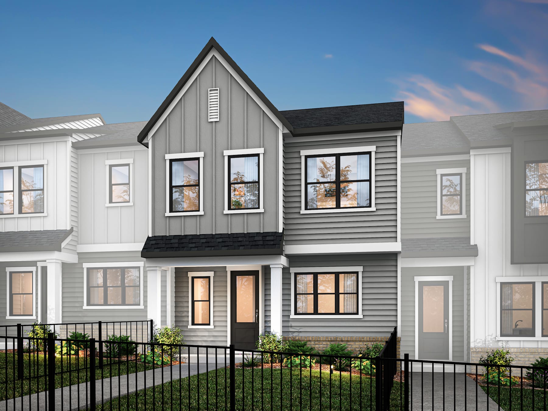 A modern, two-story townhouse with a gray exterior, black roof, and a small front yard enclosed by a metal fence, set against a clear blue sky.