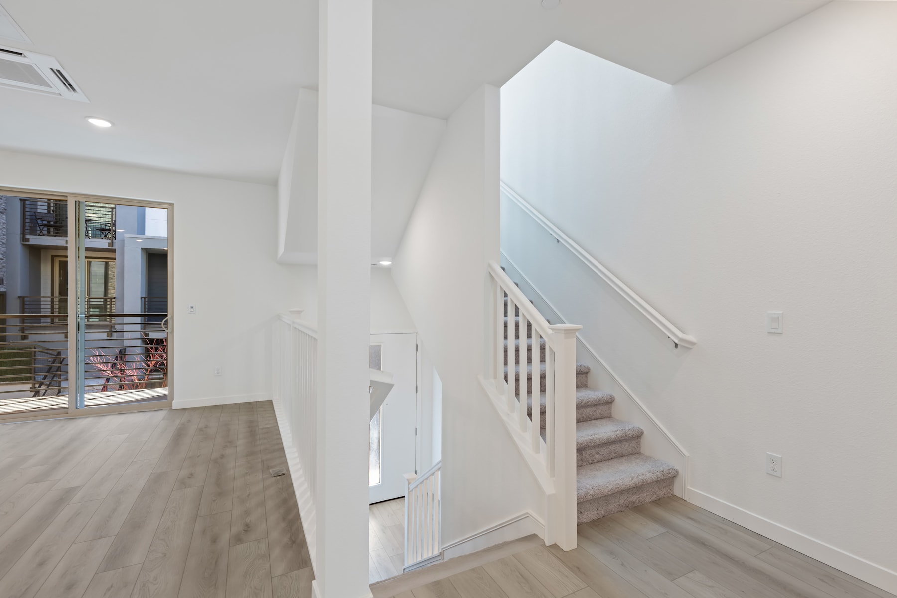 A bright and airy interior space with a staircase leading up to a second level, featuring hardwood floors and white walls.