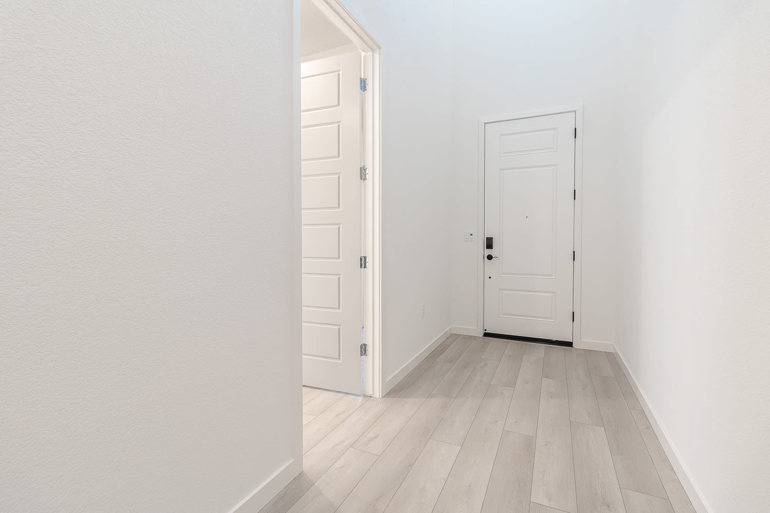A bright, minimalist hallway with white walls, a wooden floor, and a closed door at the end.